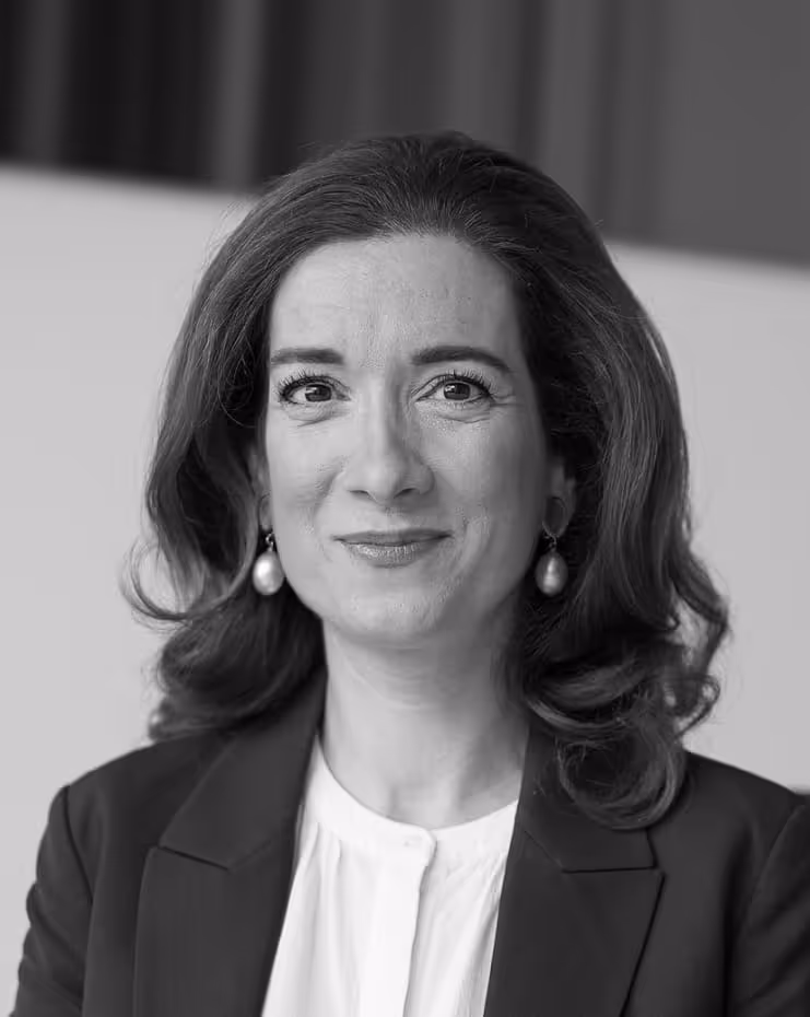 Black and white portrait of a woman with shoulder-length hair wearing pearl earrings, a white blouse, and a dark blazer, smiling slightly.